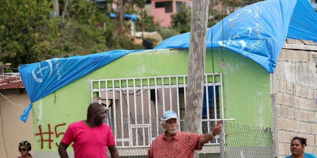 Residents stand near a house with a plastic sheet replacing the roof hit by Hurricane Maria in September.