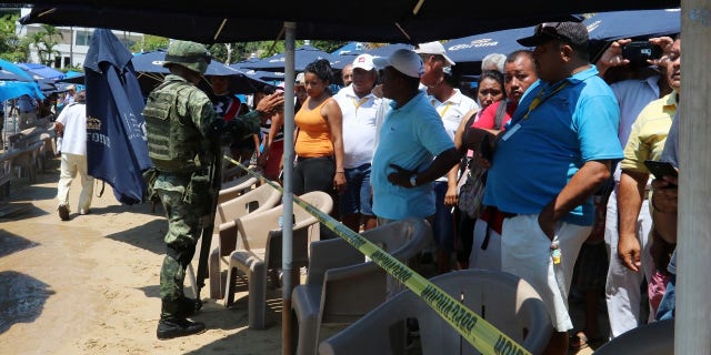 Tourist and residents look at the body of a man who washed ashore near a Mexico tourist destination.