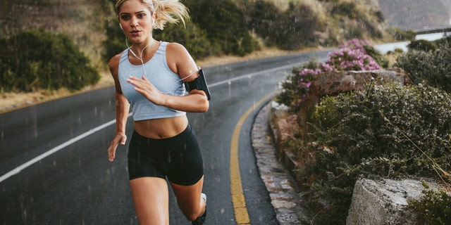 Female athlete running outdoors on highway. Beautiful young woman training running on a rainy day.