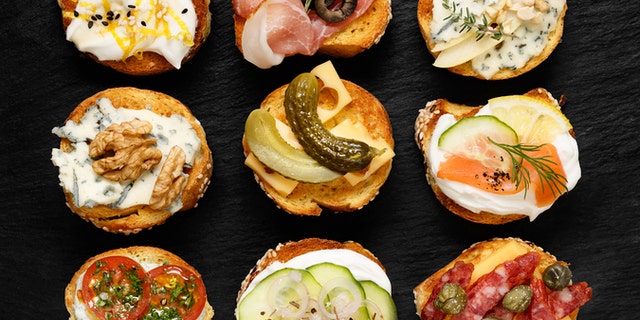 Delicious appetizers with slices of baguette and various toppings on stone black background
