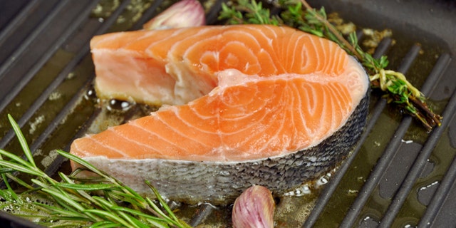 Salmon steak being fried in a pan with rosemary,thyme and garlic