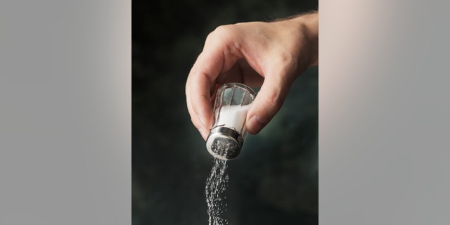 Hand adding salt using a salt shaker