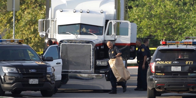 San Antonio police officers investigate the scene where eight people were found dead in a tractor-trailer loaded with at least 30 others outside a Walmart store.