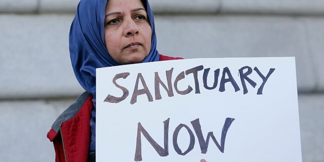 FILE - In this Jan. 25, 2017 file photo, a woman holds a sign at a rally outside of City Hall in San Francisco. The Trump administration is moving beyond rhetoric in its effort to crack down on so-called sanctuary cities that refuse to cooperate with federal immigration authorities. The Justice Department is forcing nine communities to prove they are complying with an immigration law to continue receiving coveted law enforcement grant money. (AP Photo/Jeff Chiu, File)