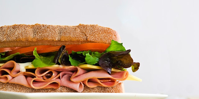 A gourmet sandwich of ham, cheese, lettuce, tomato and mayonaise isolated on white.