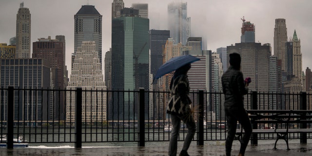 Passersby walk on the Promenade in Brooklyn Heights, New York as rain and clouds loom over Manhattan on the fifth anniversary of Hurricane Sandy.