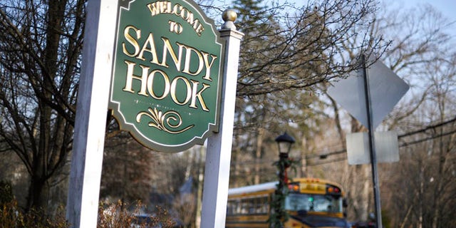 A school bus drives past a lamppost decorated for the holidays, and a sign reading Welcome to Sandy Hook, in Newtown, Conn.