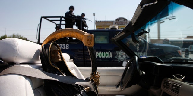 Federal police on patrol travel past a depiction of La Santa Muerte.