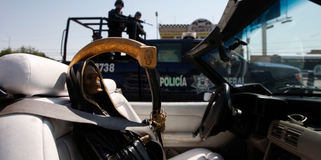 Federal police on patrol travel past a depiction of La Santa Muerte.