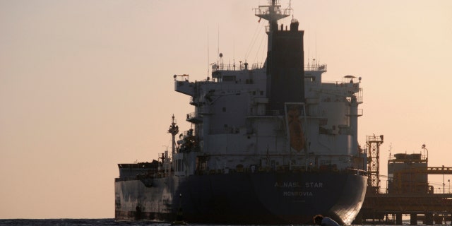 A fisherman pulls in his net as an oil tanker is seen at the port in the northwestern city of Duba April 20, 2013.