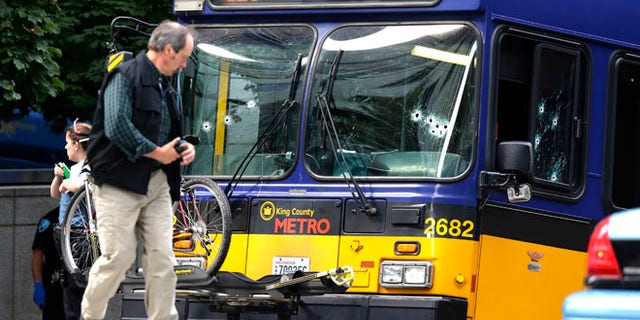Aug. 12, 2013: An official walks next to a King Co. Metro bus with multiple bullet holes in its windshield and side window, after a bus driver was shot Monday in downtown Seattle. A man who had shot the driver of another bus was shot by officers after he boarded the bus shown here.
