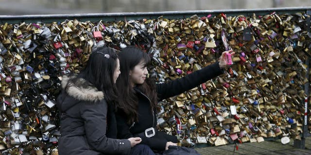 Tourists make a "selfie" picture in front of padlocks clipped by lovers on the Pont des Arts over the River Seine in Paris (REUTERS/Charles Platiau)