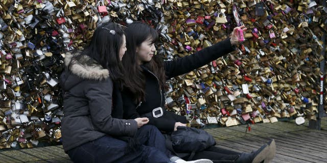 Tourists make a "selfie" picture in front of padlocks clipped by lovers on the Pont des Arts over the River Seine in Paris (REUTERS/Charles Platiau)