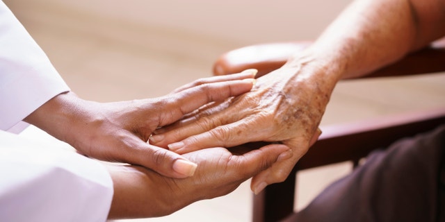 Old people in geriatric hospice: Aged patient receives the visit of a female black doctor. They shake their hands and talk in the hospital.