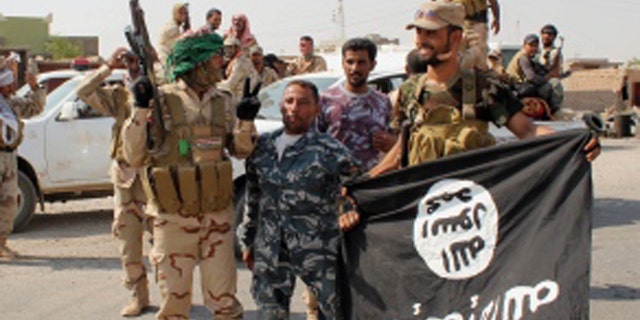 Shia militias, shown here in 2014 holding a captured ISIS flag from an operation near Baghdad, have been accused by Amnesty International of operating outside the law.