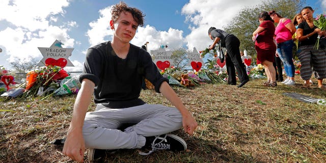 FILE- In this Feb. 19, 2018, file photo, Chris Grady, a student at Marjory Stoneman Douglas High School, sits at a memorial in Parkland, Fla., for those slain in the Feb. 14 school shooting. Grady who had planned to join the U.S. Army before the shooting, has withdrawn his enlistment and will now work for the March for Our Lives movement. (AP Photo/Gerald Herbert, File)