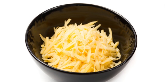Grated cheddar cheese in a black bowl, isolated on white.