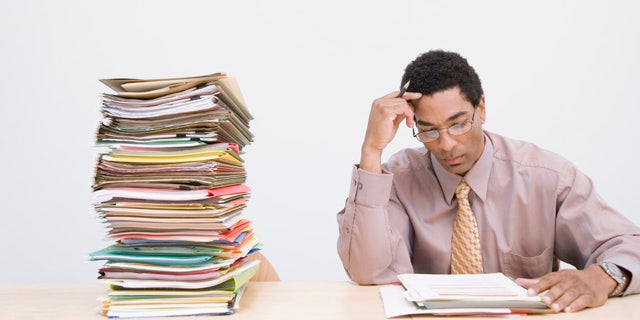 Businessman sitting next to stack of documents on desk, clocks on wall