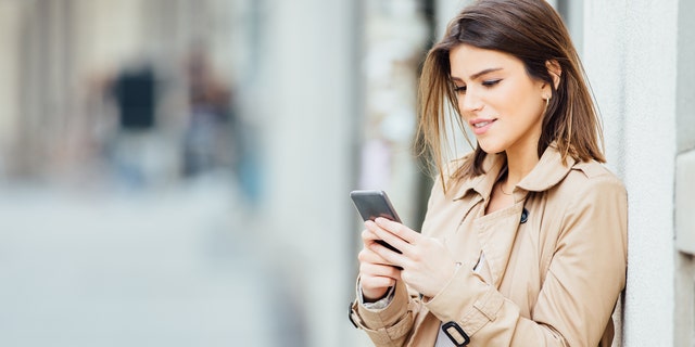 Beautiful young woman standing at the street and using her mobile phone