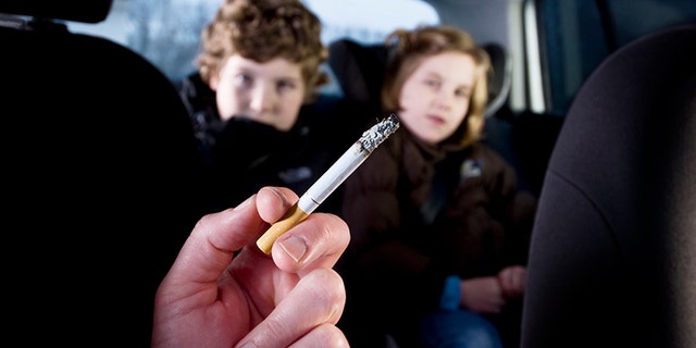 Two young children being subjected to the effects of passive smoking from their mother's cigarette.