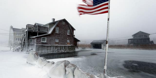 A tattered flag flies by a flooded yard along the shore in Scituate, Mass., Friday, Jan. 3, 2014. A blustering winter storm that dropped nearly 2 feet of snow just north of Boston, shut down major highways in New York and Pennsylvania and forced U.S. airlines to cancel thousands of flights nationwide menaced the Northeast on Friday with howling winds and frigid temperatures. (AP Photo/Michael Dwyer)