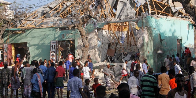 Somalis stand outside a destroyed building after a car bomb in Mogadishu, Somalia, March 22, 2018.