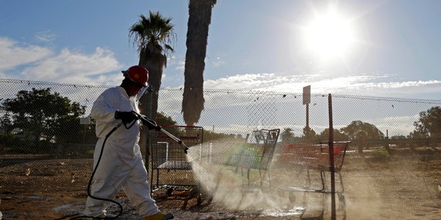 In this Sept. 25, 2017 photo, a worker sprays a bleach solution on a sidewalk in downtown San Diego as part of an effort to control a deadly hepatitis A outbreak.