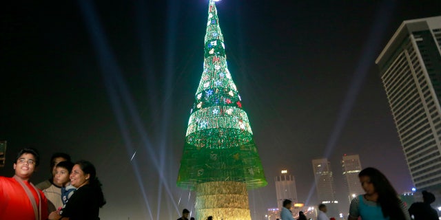 A Sri Lankan family takes photographs standing near an enormous artificial Christmas tree as others gather around it in Colombo, Sri Lanka, Saturday, Dec. 24, 2016.