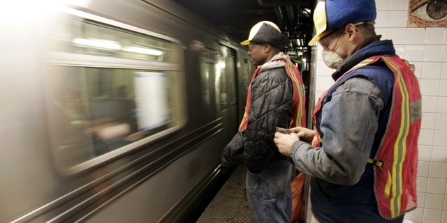 New York City Transit workers watch as an A subway train enters the Chambers Street station, Tuesday Jan. 25, 2005, near the scene of a fire apparently set by a homeless person Sunday, that spread to a vital equipment room. Hundreds of thousands of riders on two of the city's busiest subway lines face significant delays and overcrowding lasting up to five years. (AP Photo/Richard Drew)