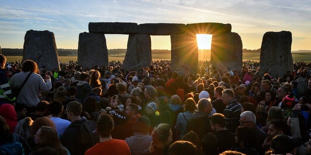 The sun rises through the stones at Stonehenge as crowds of people gather to celebrate the dawn of the longest day in the UK, in Wiltshire, England, Thursday June 21, 2018. The neolithic Wiltshire monument is built along the solstice alignment of the summer sunrise and the winter sunset. (Ben Birchall/PA via AP)