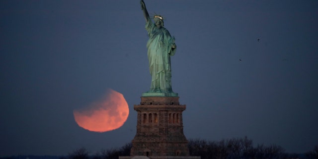 The Statue of Liberty is backdropped by a supermoon, Wednesday, Jan. 31, 2018, seen from the Brooklyn borough of New York. The supermoon, which is the final of three consecutive supermoons, also experience lunar eclipse as it set over the horizon, but only a partial eclipse was visible in the East Coast. (AP Photo/Julio Cortez)