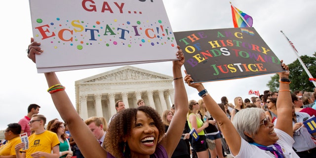 Ikeita Cantu, left, and her wife Carmen Guzman, of McLean, Virginia, hold up signs as they celebrate outside the Supreme Court in Washington, D.C., Friday, June 26, 2015, after the court declared that same-sex couples have a right to marry anywhere in the U.S.