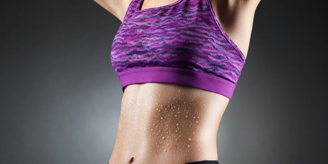 Fit anonymous sport-girl in black yoga pants and purple top with heat droppings on abdominal muscles. Studio portrait black background.