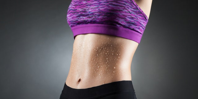 Fit anonymous sport-girl in black yoga pants and purple top with heat droppings on abdominal muscles. Studio portrait black background.