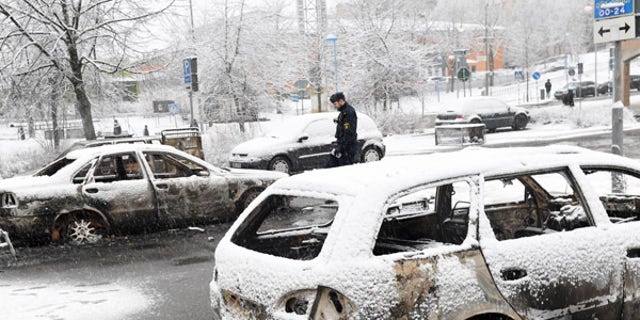 A policeman investigates a burned car in the suburb of Rinkeby on Monday.