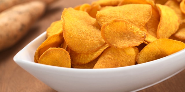 Crispy Peruvian sweet potato chips in white ceramic bowl with sweet potatoes in the back (Selective Focus, Focus one third into the sweet potato chips)