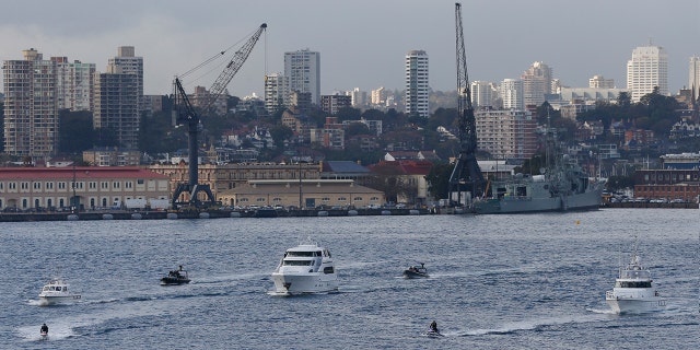 A flotilla including a motor launch crosses Sydney Harbor.