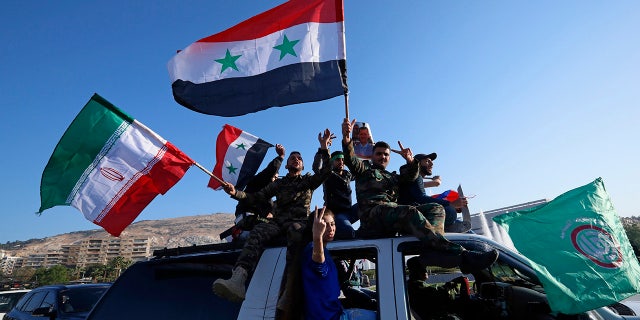 Syrian government supporters wave Syrian, Iranian and Russian flags as they chant slogans against U.S. President Trump.