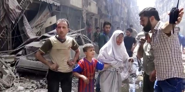 In this image made from video and posted online from Validated UGC, a man leads a woman in tears and child out of the scene after airstrikes hit Aleppo, Syria, Thursday, April 28, 2016.