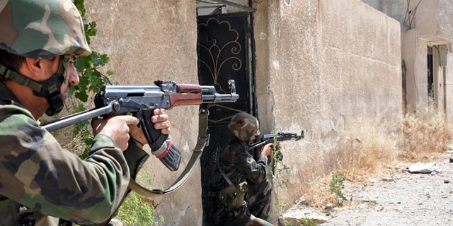 In this photo released on June 5, 2013 by the Syrian official news agency SANA, Syrian soldiers loyal to President Bashar Assad aim their weapons in an area near the Homs-Damascus highway, central Syria. Syrian troops and their Lebanese Hezbollah allies captured a strategic border town Wednesday after a grueling three-week battle, dealing a severe blow to rebels and opening the door for President Bashar Assad's regime to seize back the country's central heartland.