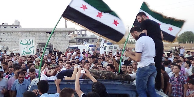 In this citizen journalism image provided by Shaam News Network SNN, taken on Tuesday, Aug. 7, 2012, Syrians attend the funeral procession of a man killed in Idlib province, Syria. Arabic, left, reads, "God is great."