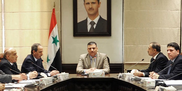 In this undated photo released by the Syrian official news agency SANA on Sunday, Aug. 5, 2012, Syrian Prime Minister Riad Hijab, center, speaks under the portrait of the Syrian President Bashar Assad during a meeting in Damascus, Syria. Hijab defected and fled to neighboring Jordan, a Jordanian official and a rebel spokesman said Monday, Aug. 6, 2012.
