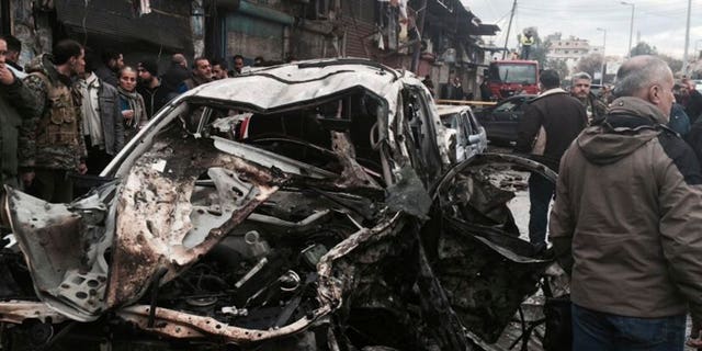 In this photo released by the Syrian official news agency SANA, Syrian citizens gather next to damaged cars at the scene where explosion hit a commercial street, in the costal town of Jableh, Syria, Thursday, Jan. 5, 2017. A large explosion hit a Syrian government-held coastal town on Thursday, killing and wounding several people, according to Syria's state TV an attack that undermined a nearly week-old and already shaky Russia- and Turkey-brokered cease-fire. (SANA via AP)