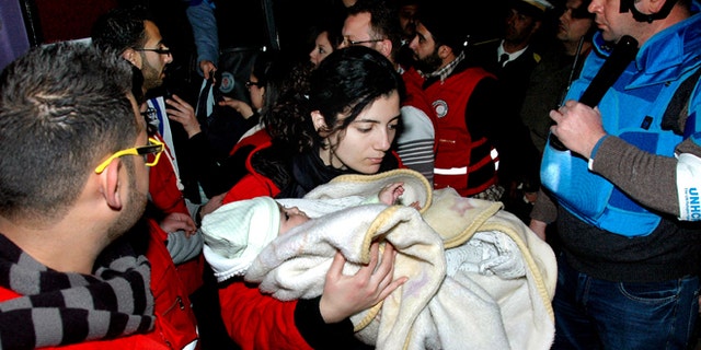Feb. 10, 2014: In this photo released by the Syrian official news agency SANA, a Syrian Arab Red Crescent member in red uniform carries a baby on to a bus to evacuate the battleground city of Homs, Syria.