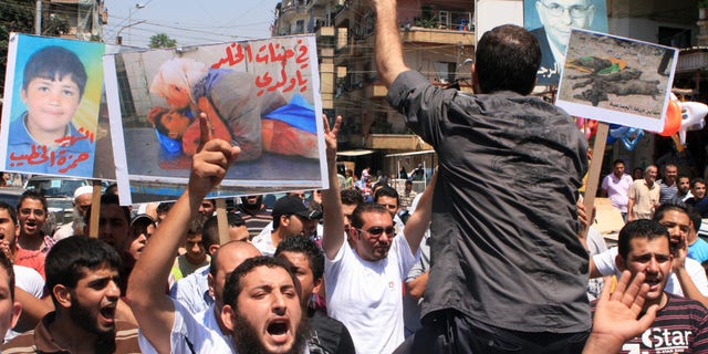 Lebanese protesters shout slogans as they carry banners in Arabic that read:" you are in heaven my son," center, "the martyr Hamza el-Khatib," left, and " Daraa mass graves," right, during a rally in solidarity with Syrian anti-government protesters in the northern city of Tripoli, Lebanon, Friday, July 15, 2011.