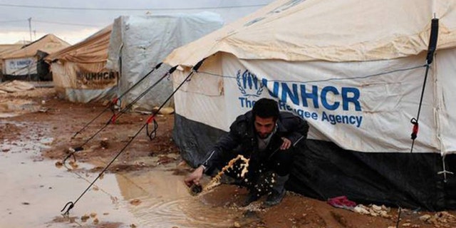 A Syrian refugee removes water and mud around his UN-supplied tent, at Zaatari Syrian refugee camp, near the Syrian border in Mafraq, Jordan.