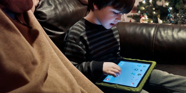 In this Dec. 3, 2013, photo, Adam Cohen watches as his son Marc, 5, uses a tablet at their home in New York. Tablets of all types are expected to rank among the top holiday gifts for children this year, but some experts and advocates question the educational or developmental benefits for youngsters. (AP Photo/Bebeto Matthews)