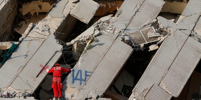 An emergency rescue worker searches what was the 14th floor of a collapsed building in Tainan, Taiwan, Sunday, Feb. 7, 2016. Rescuers on Sunday found signs of live within the remains of a high-rise residential building that collapsed in a powerful, shallow earthquake in southern Taiwan that killed over a dozen people and injured hundreds. (AP Photo/Wally Santana)