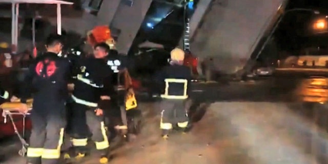 In this image from TV, emergency services attend after a building collapsed on its side, as a man climbs a ladder to gain access to the building, center background, after an early morning earthquake in Hualien County, eastern Taiwan.