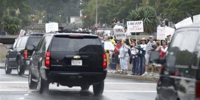Sunday: President Obama's motorcade drives towards the White House past Tea Party protesters.